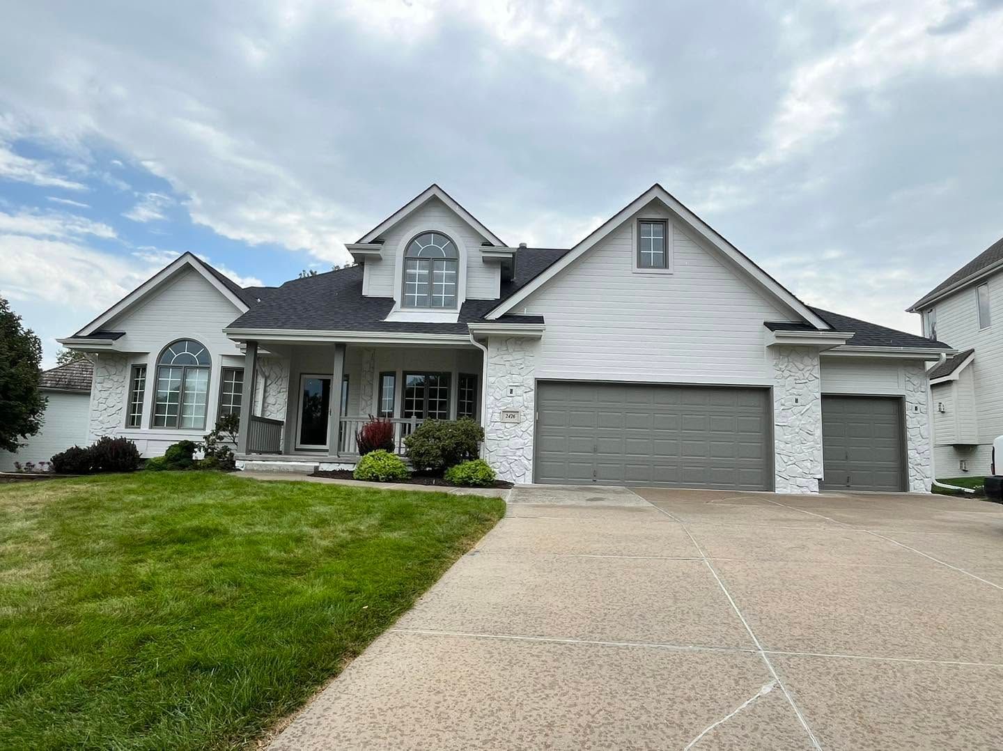 Suburban single-story house with a gray roof, brick exterior, and large front lawn under a cloudy sky