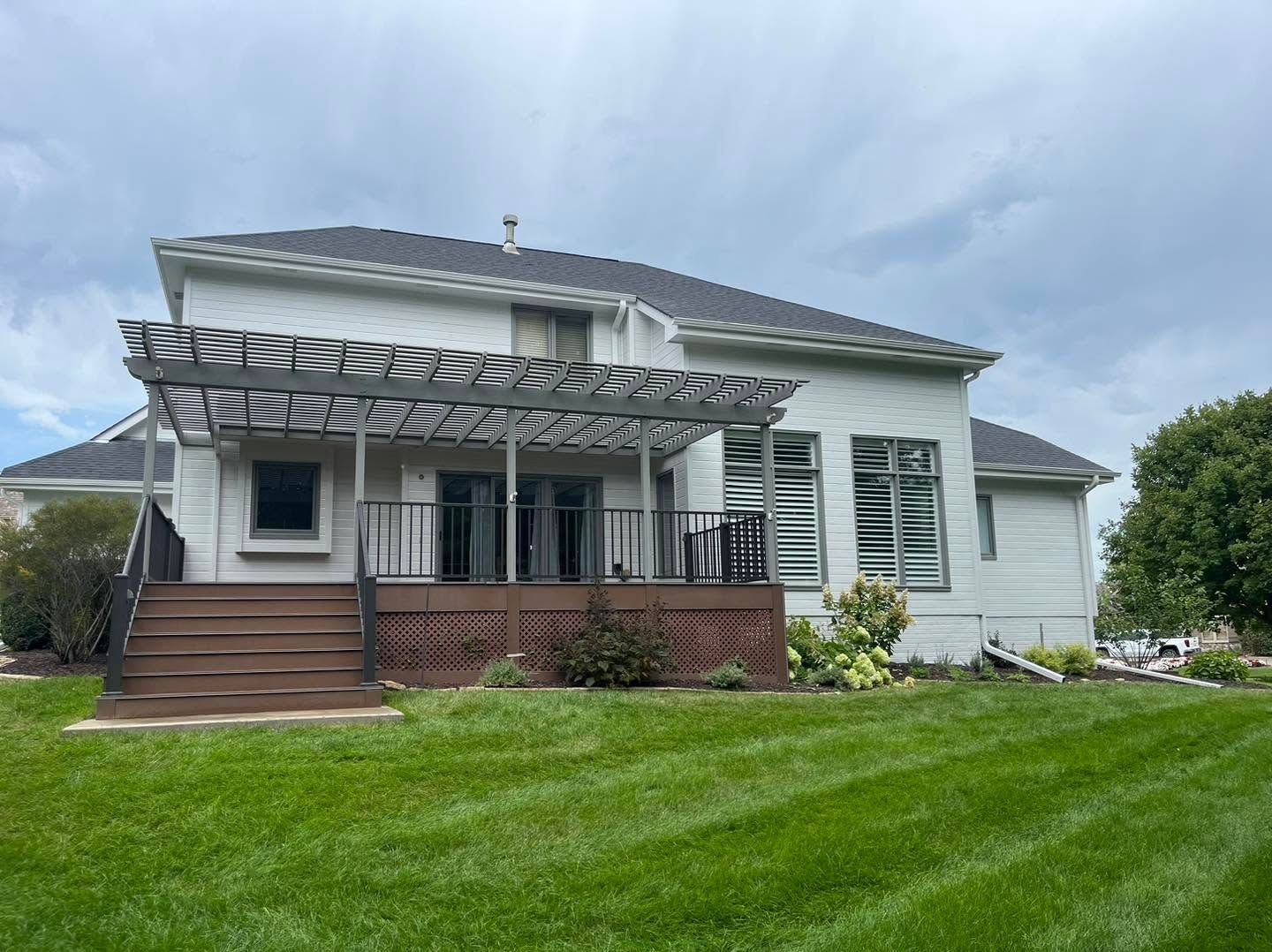 White house with screened porch, wooden steps, and lush green lawn under a cloudy sky