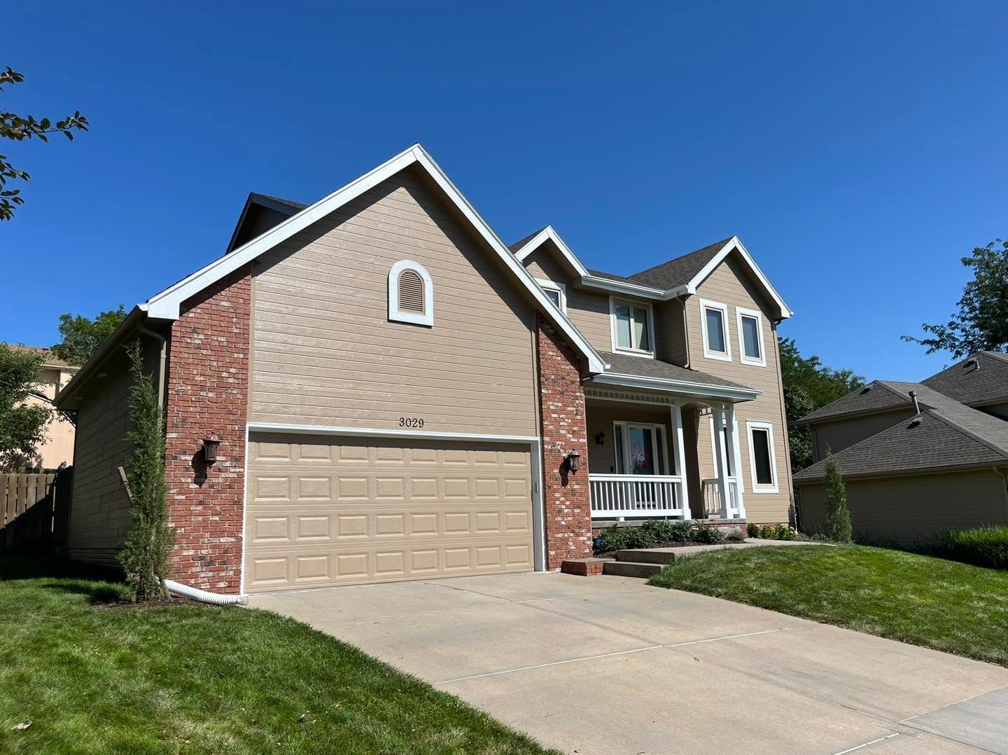 Suburban two-story brick and tan house with attached garage, driveway, and green lawn under a blue sky