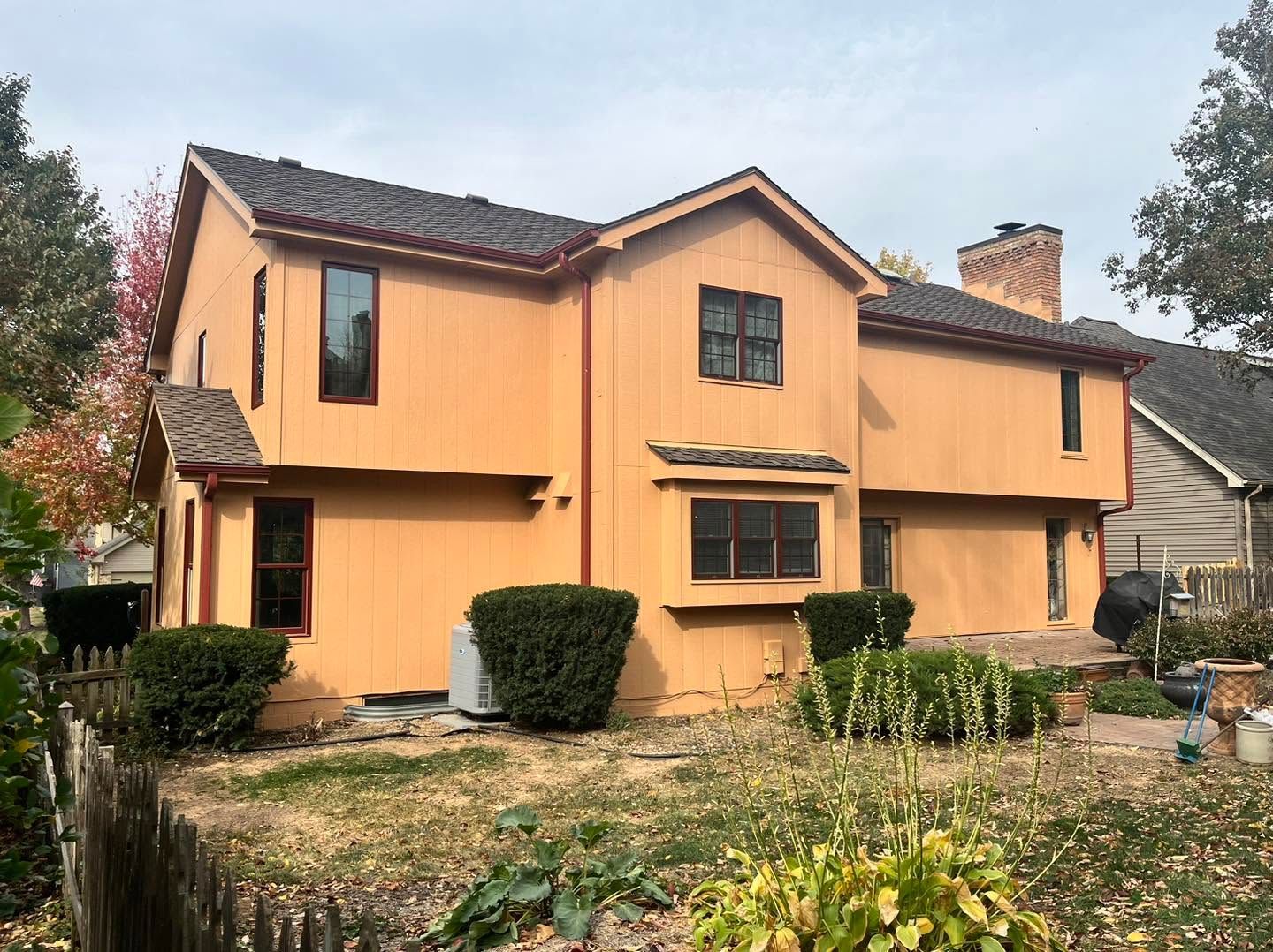 Two-story peach house with a tiled roof, front shrubs, and a garden under a cloudy sky
