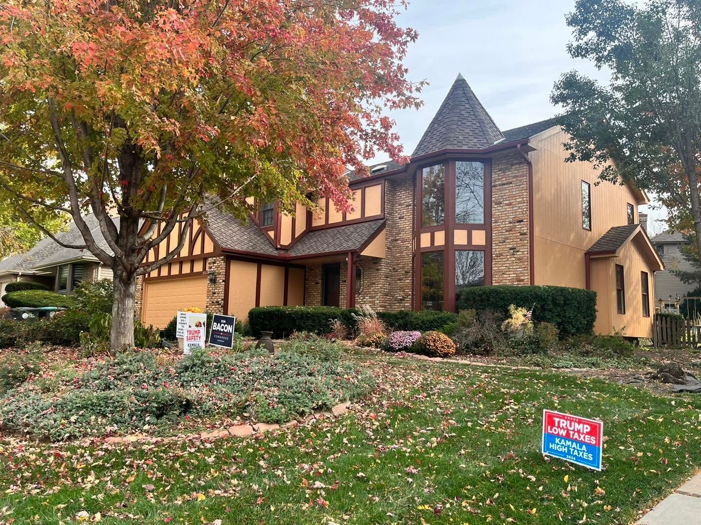 Tudor-style house with autumn trees, stone accents, and a landscaped yard with a for-sale sign