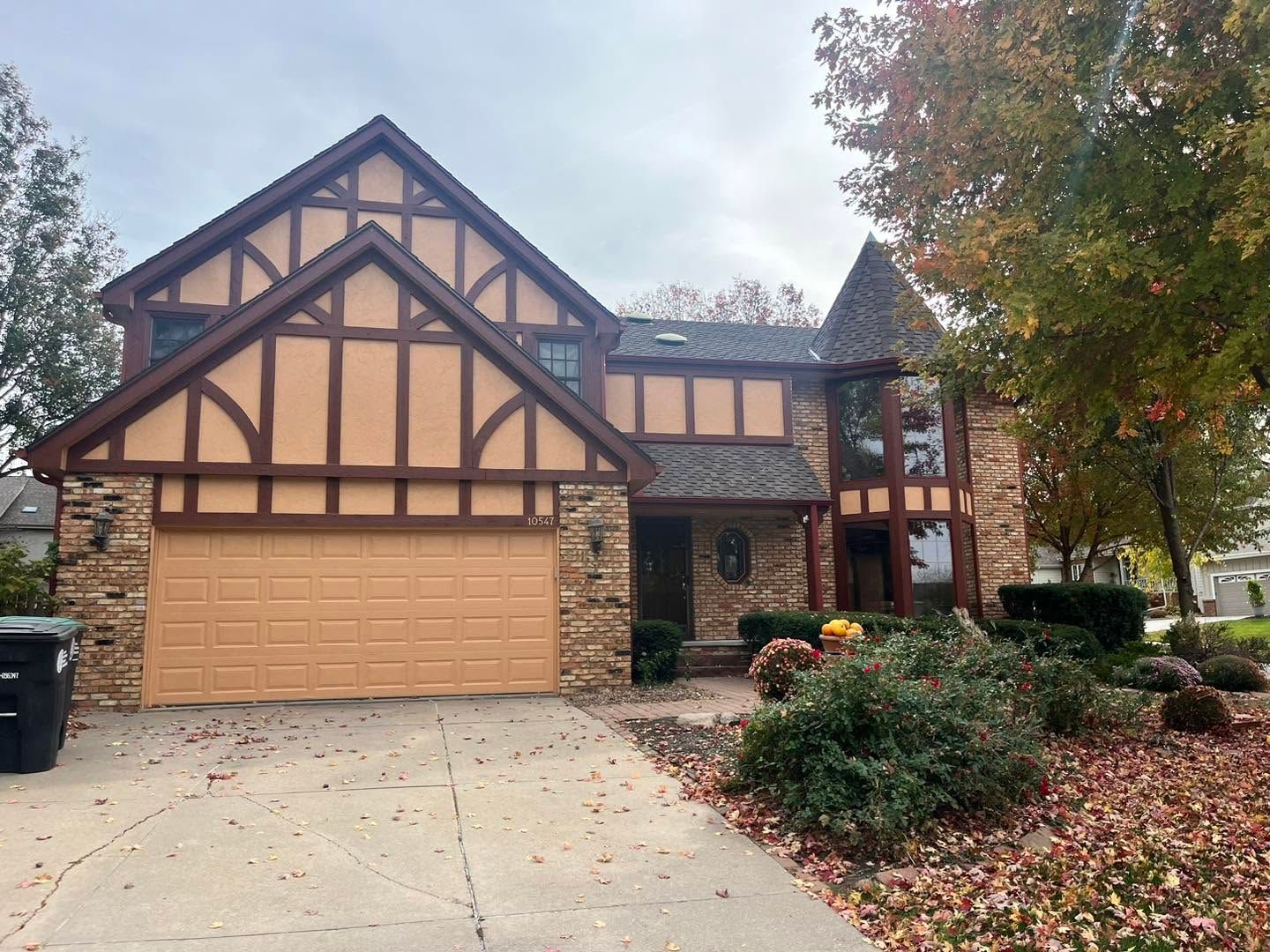 Two-story Tudor-style house with tan garage, stone accents, and autumn trees along the driveway