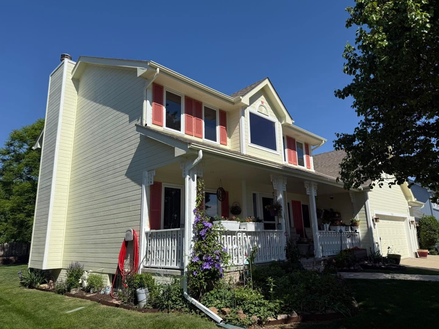 Two-story cream house with red shutters and a front porch under a clear blue sky
