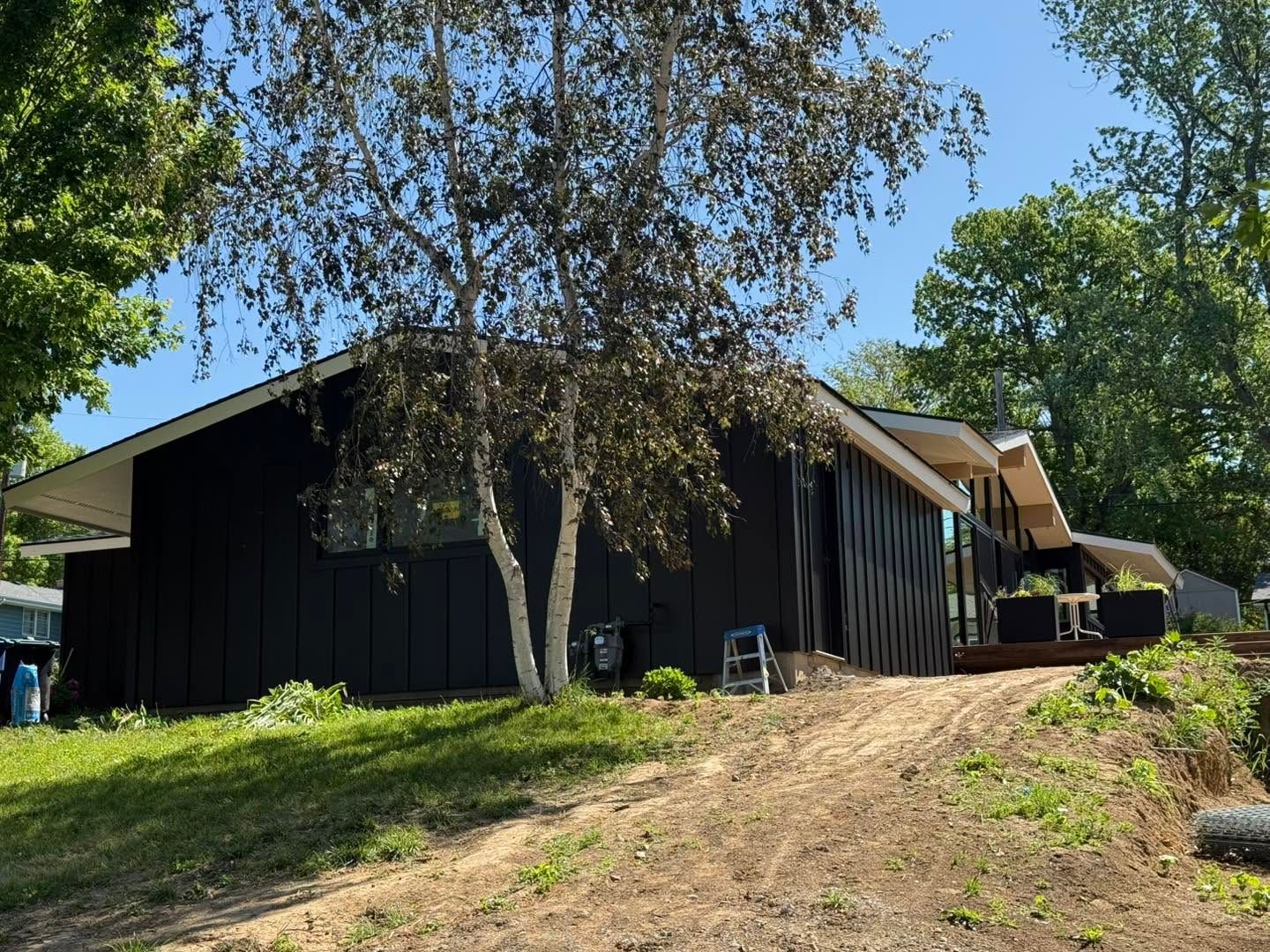 Black house on a dirt slope with trees and blue sky, seen from below