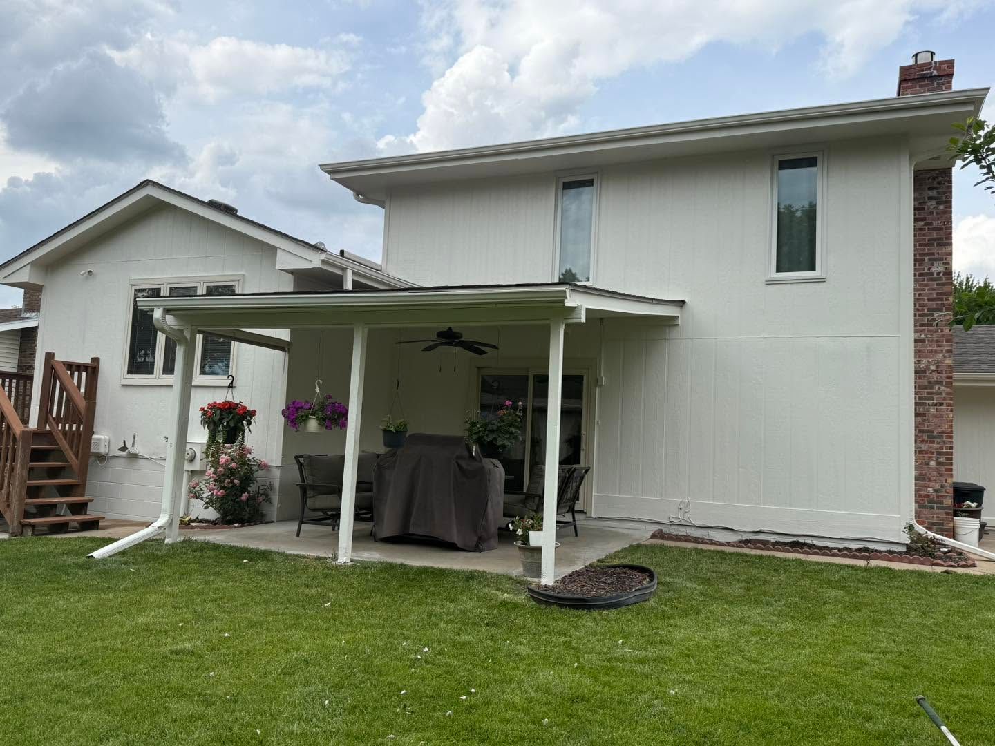 Backyard view of a white two-story house with a covered patio and green lawn