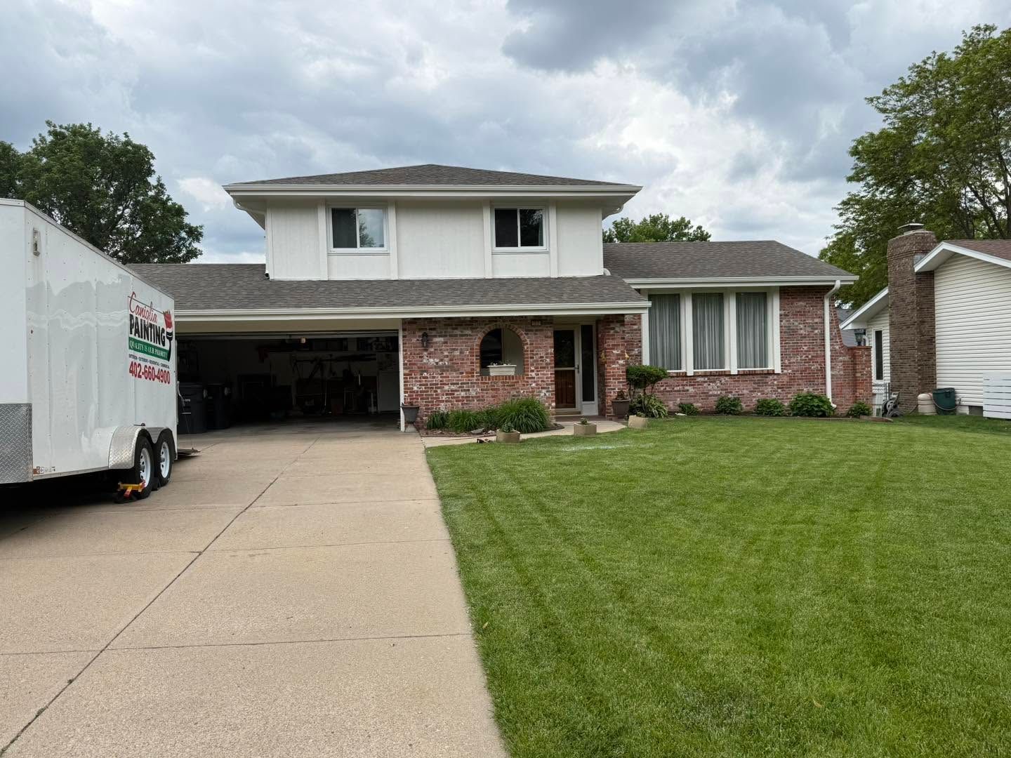 Suburban two-story brick house with a driveway, green lawn, and a truck parked on the left