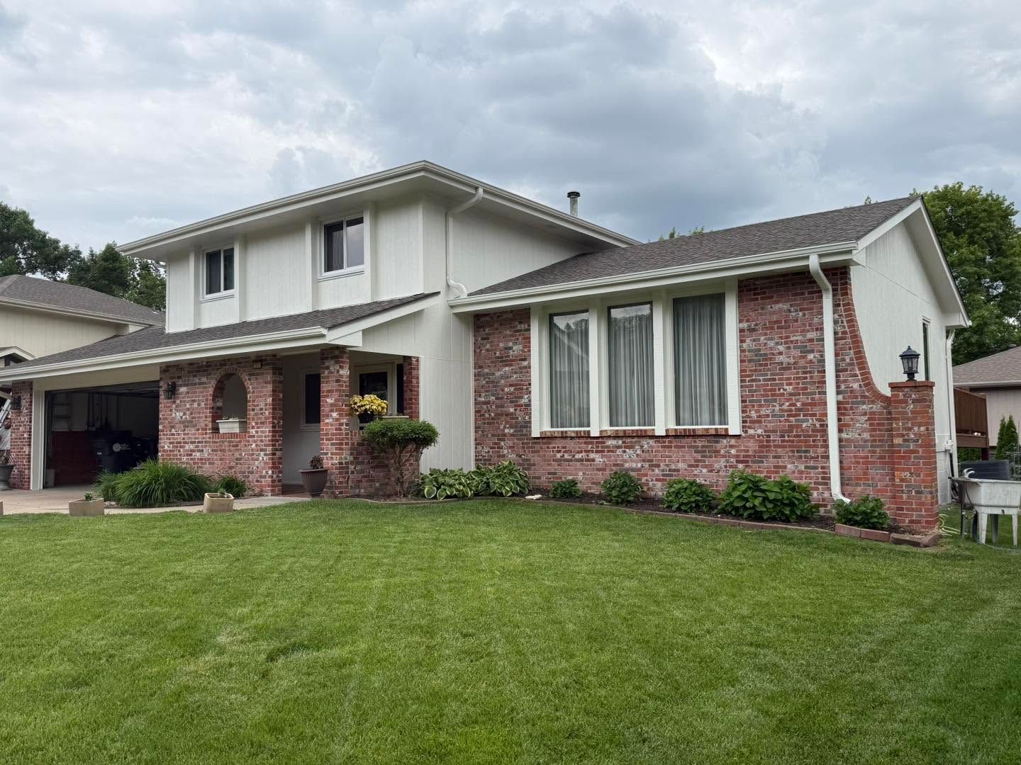 Two-story suburban house with brick and white siding, front lawn, and cloudy sky
