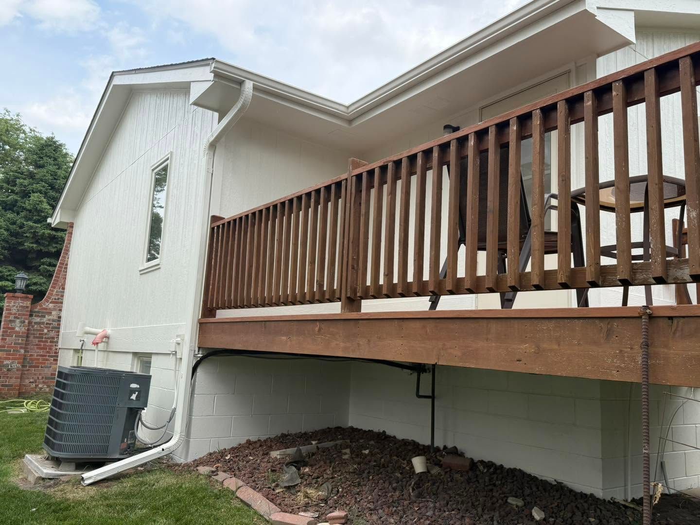 White house with a raised wooden deck and railings, showing the underside support and gravel ground below.