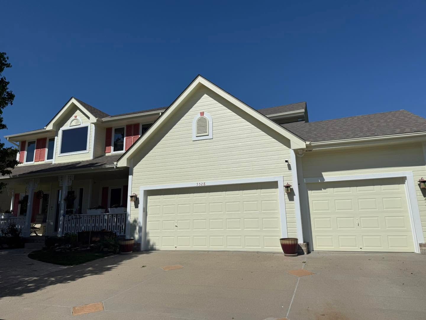 Suburban house with beige siding, garage doors, and a front porch under a blue sky