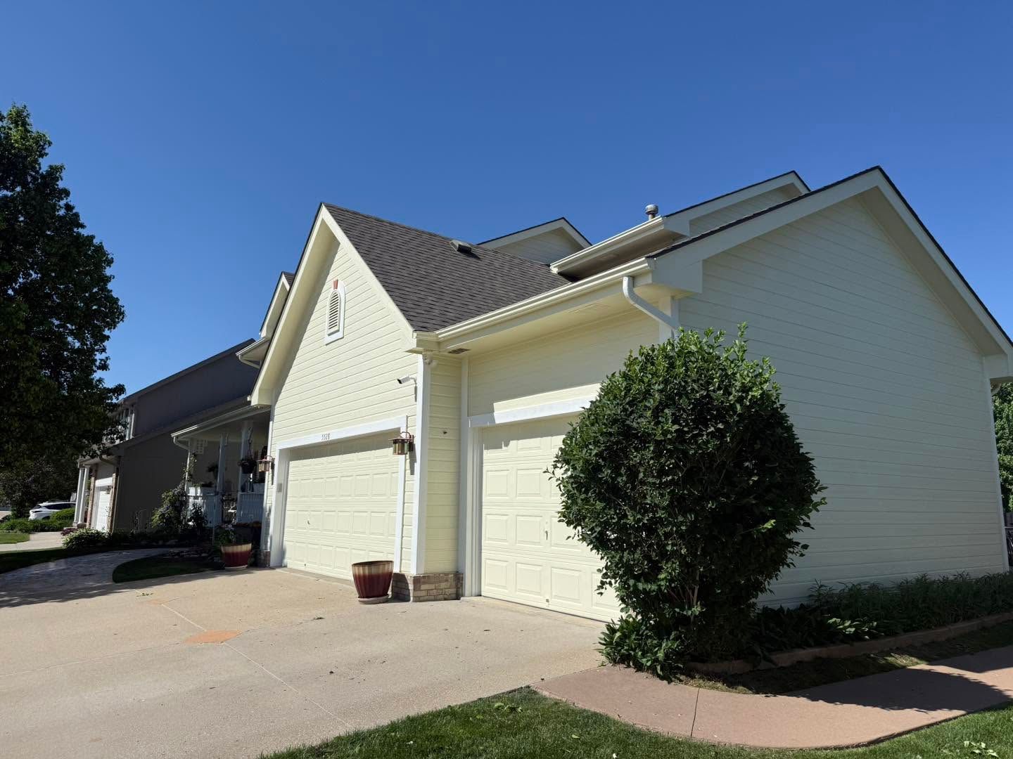 Suburban white house with attached garage, driveway, and trimmed bushes under a blue sky