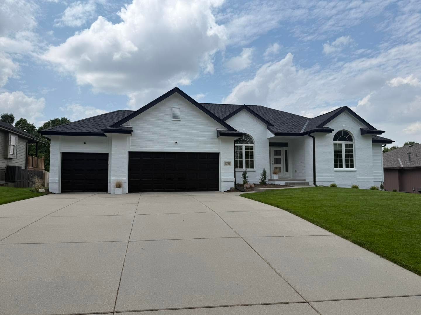 White suburban house with a three-car garage, large driveway, and green lawn under a cloudy sky