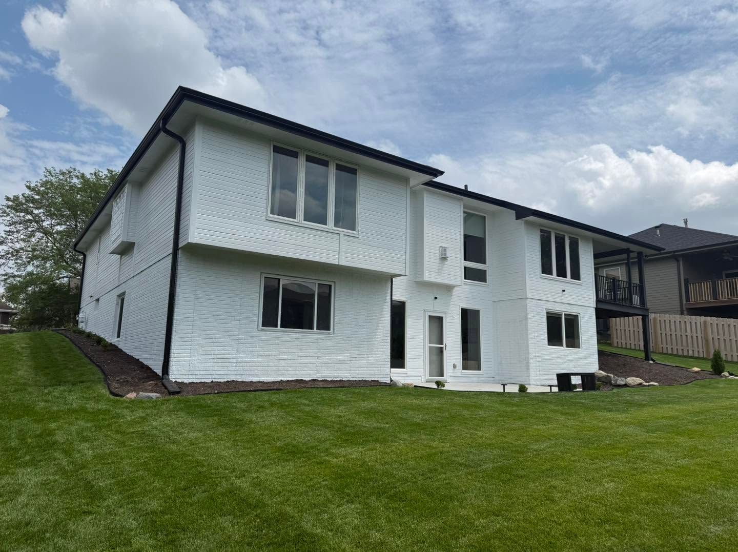 White two-story house with black trim on a green lawn under a cloudy sky
