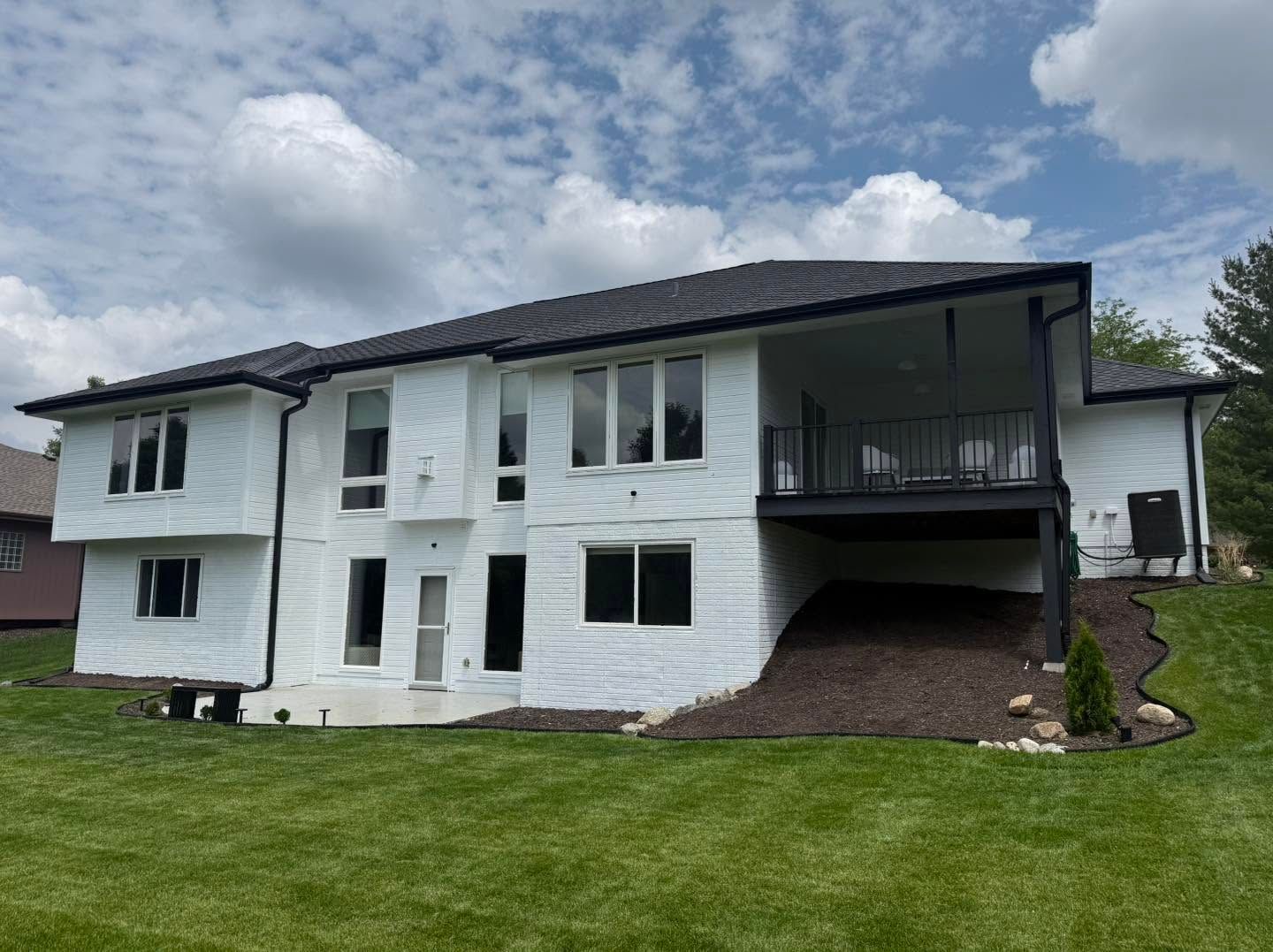 White two-story house with black roof and carport on a green lawn under a cloudy sky