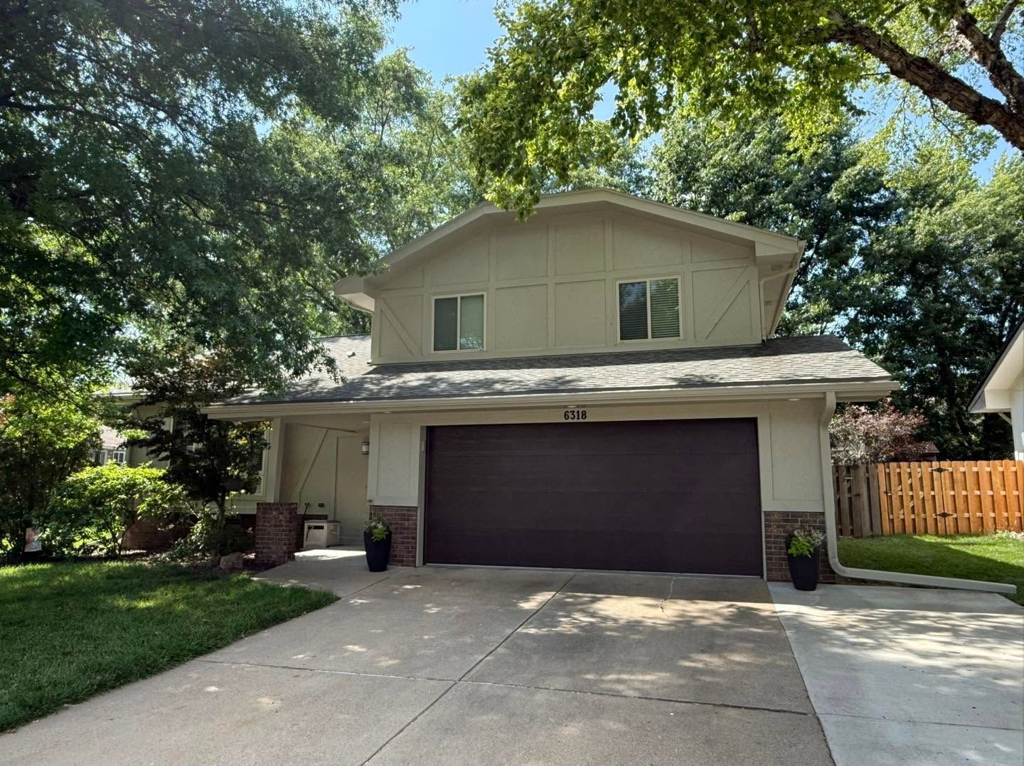 Suburban two-story house with a dark garage door, driveway, and trees shading the front yard