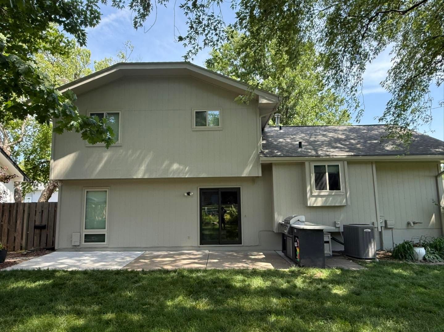 Two-story beige house with a backyard patio, trees overhead, and lawn in front