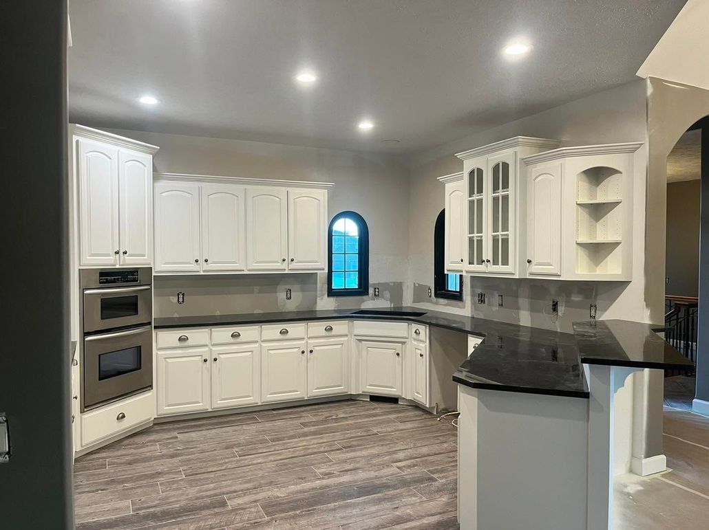 Bright modern white kitchen with dark countertops, built-in ovens, and arched windows