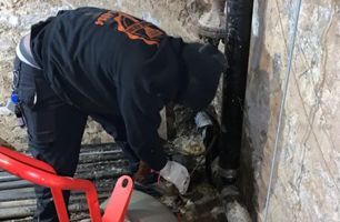 A man in a black hoodie is working on a pipe.