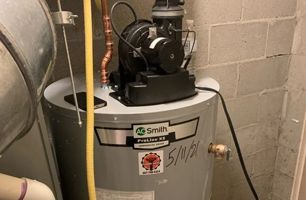 A water heater is sitting in a room next to a brick wall.