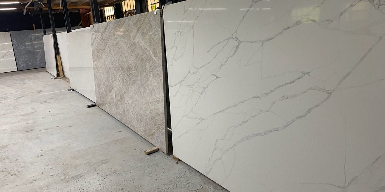 Stone slabs leaning against each other in a warehouse. White, gray, and beige colors with various veining patterns.