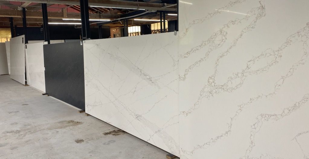 Slabs of various countertop materials, including a white one with gold veining, on display in a warehouse.