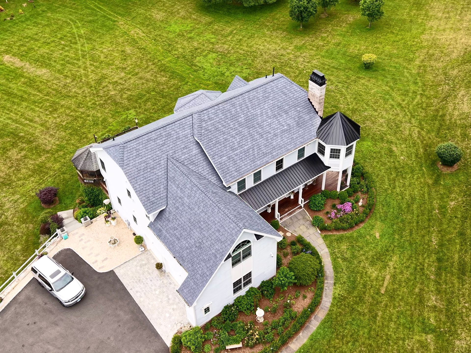 Aerial view of a white house with a gray roof and a circular tower, set in a grassy yard.