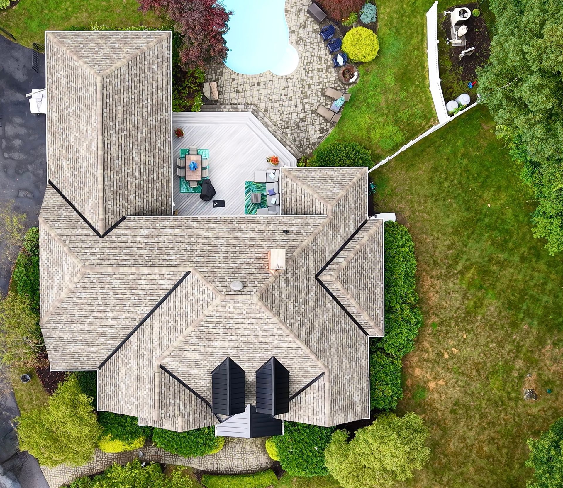 Overhead view of a house with a gray roof, pool, deck, and green lawn.