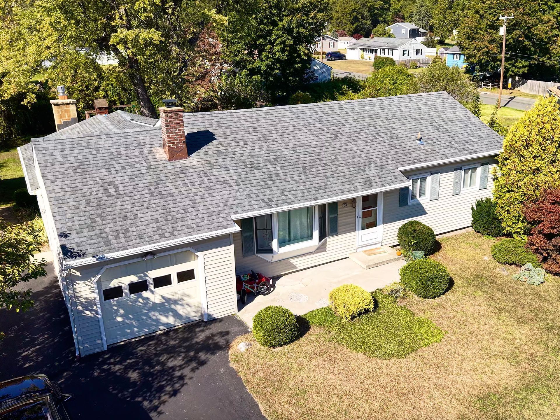 Gray ranch-style house with a chimney and attached garage on a grassy lot with a driveway.
