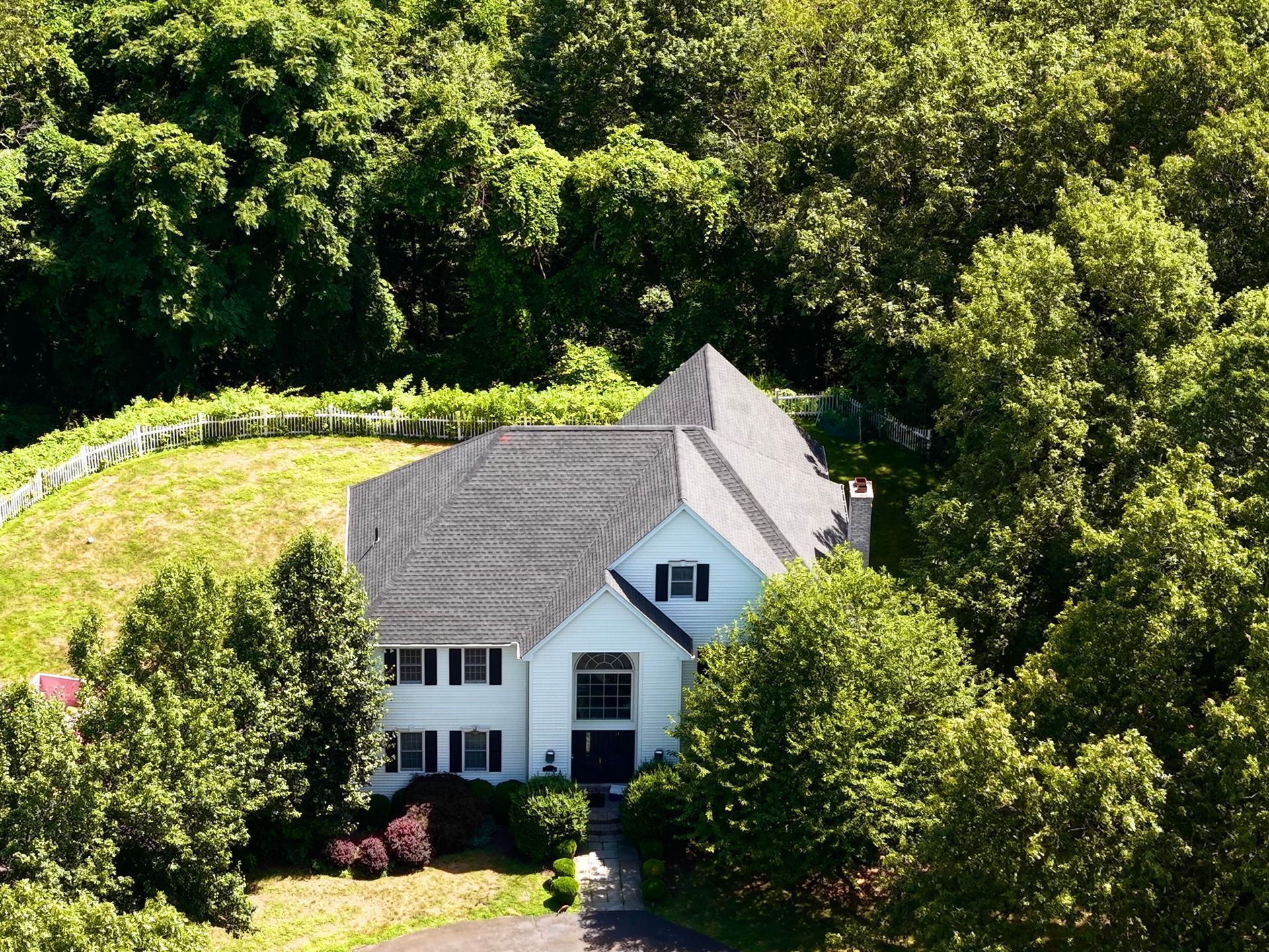 White house with gray roof surrounded by green trees and a hillside in the background.