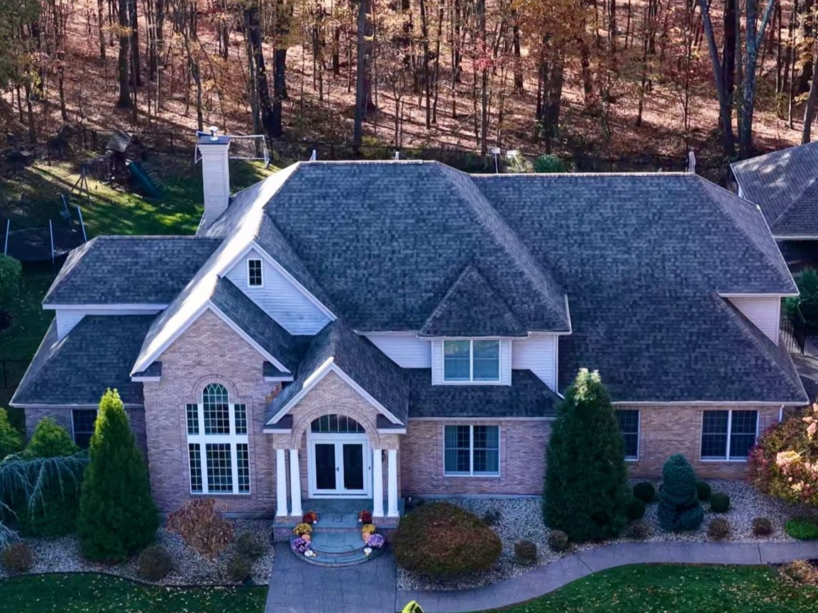 Brick home with gray roof, set against a backdrop of autumn trees.