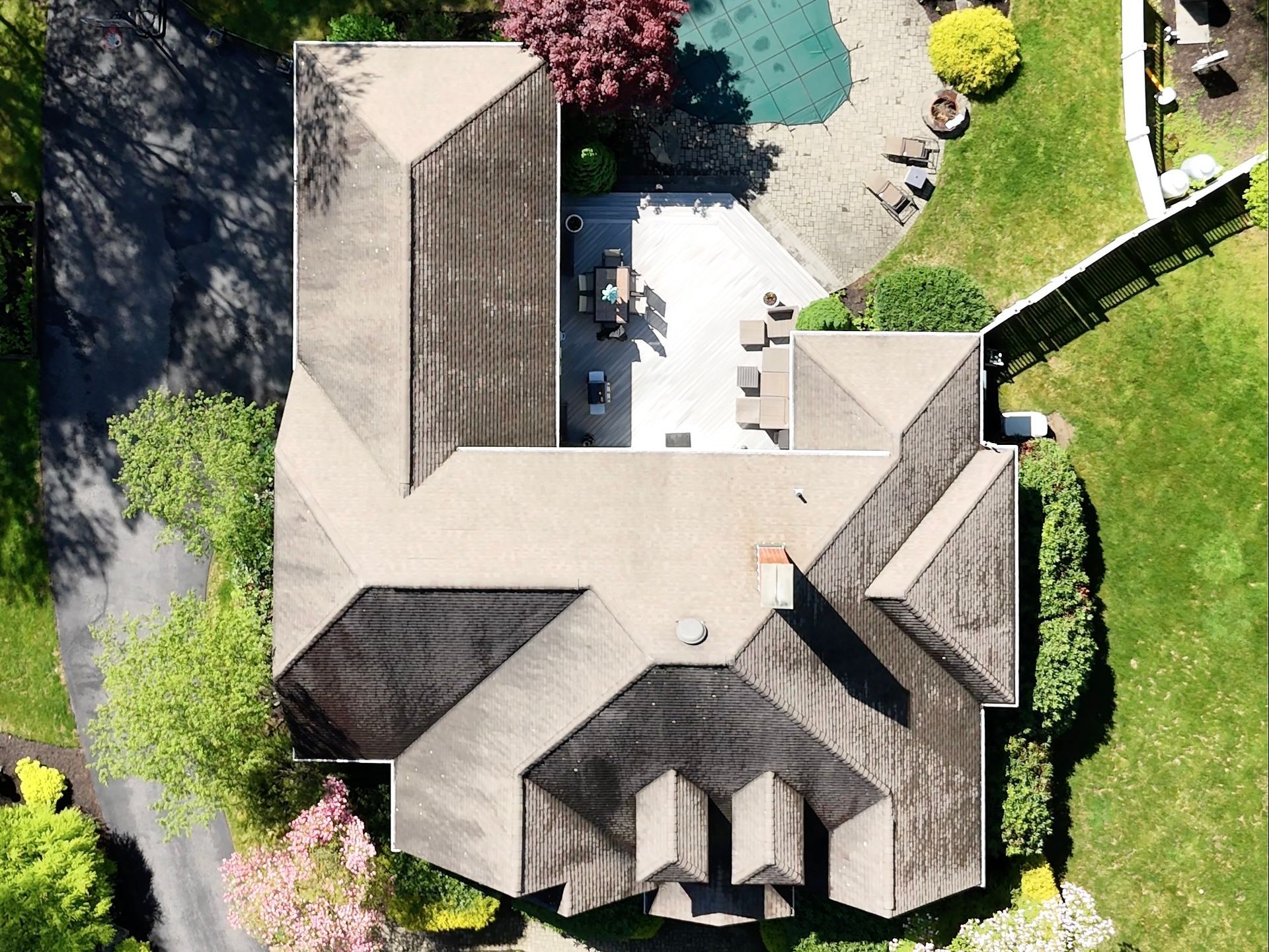 Overhead view of a house with a brown roof, patio, and swimming pool surrounded by green lawn.