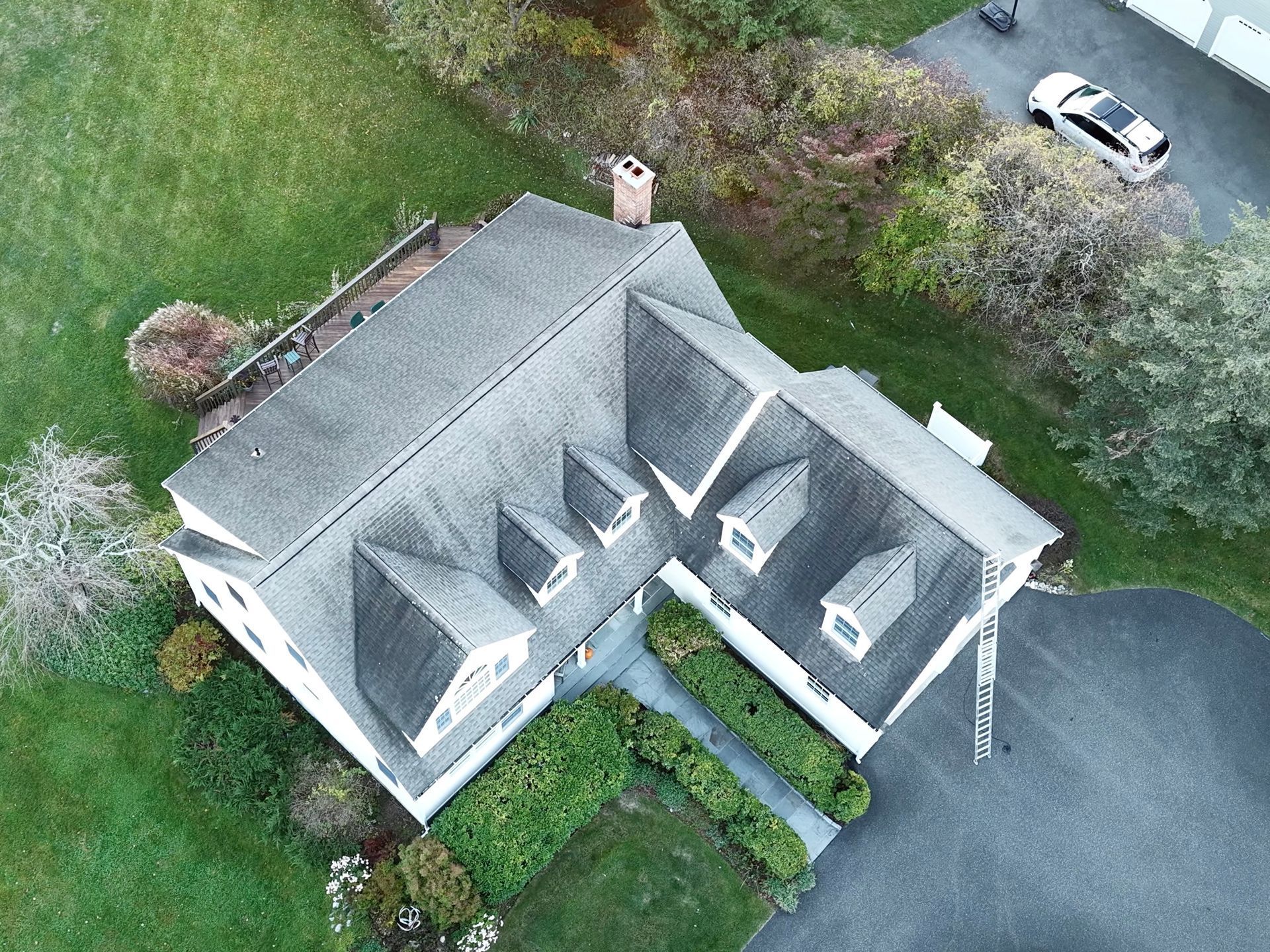 Overhead view of a white house with a gray roof and dormers, surrounded by green grass and trees.