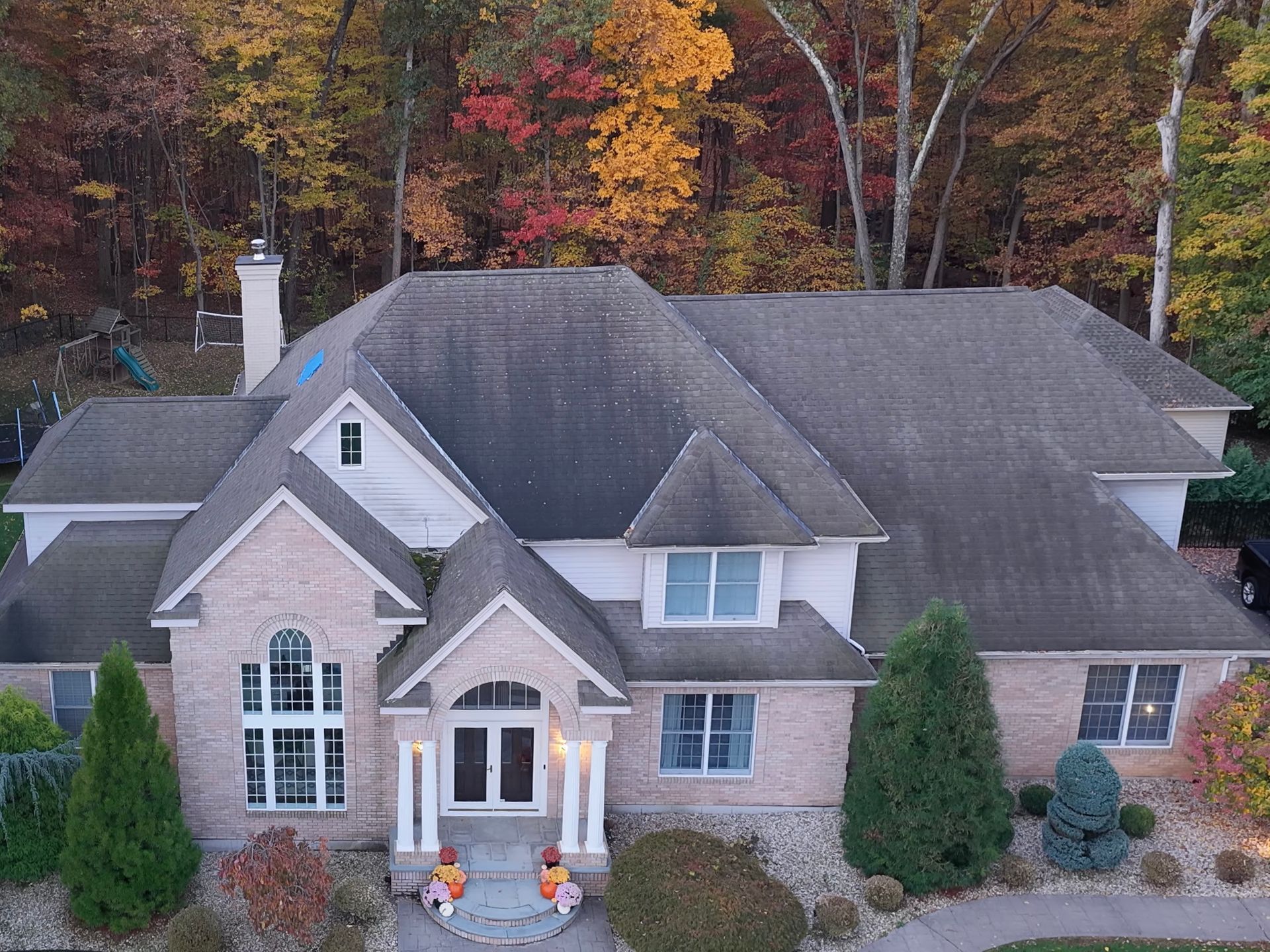 Large, two-story house with a brick facade and dark roof, surrounded by fall foliage.