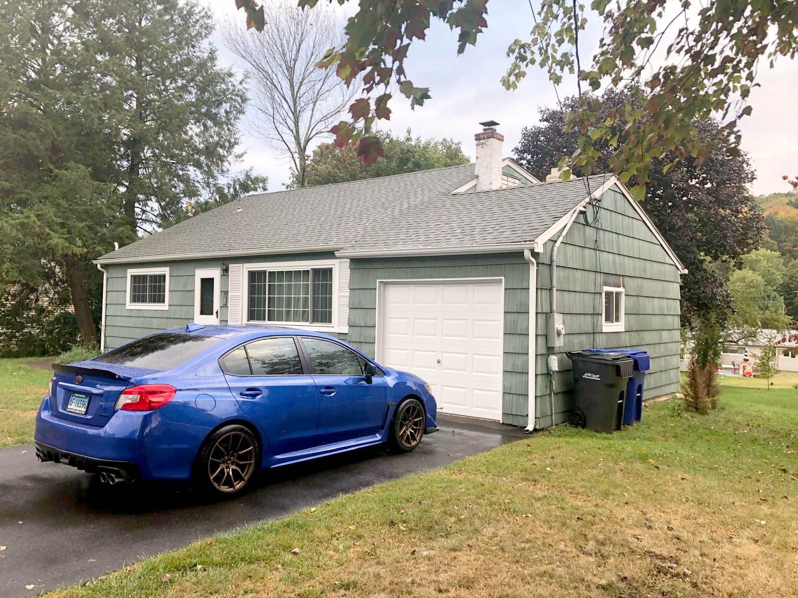 A blue car is parked in front of a small house