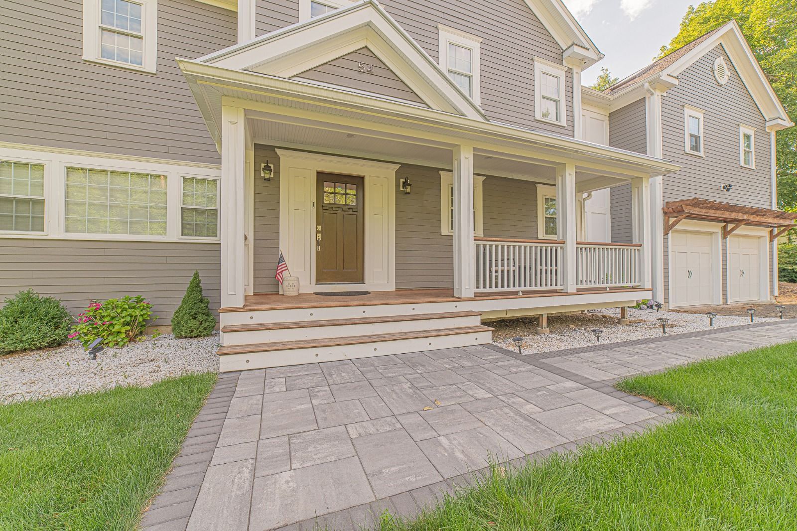 A large gray house with a large porch and a brick walkway leading to it.