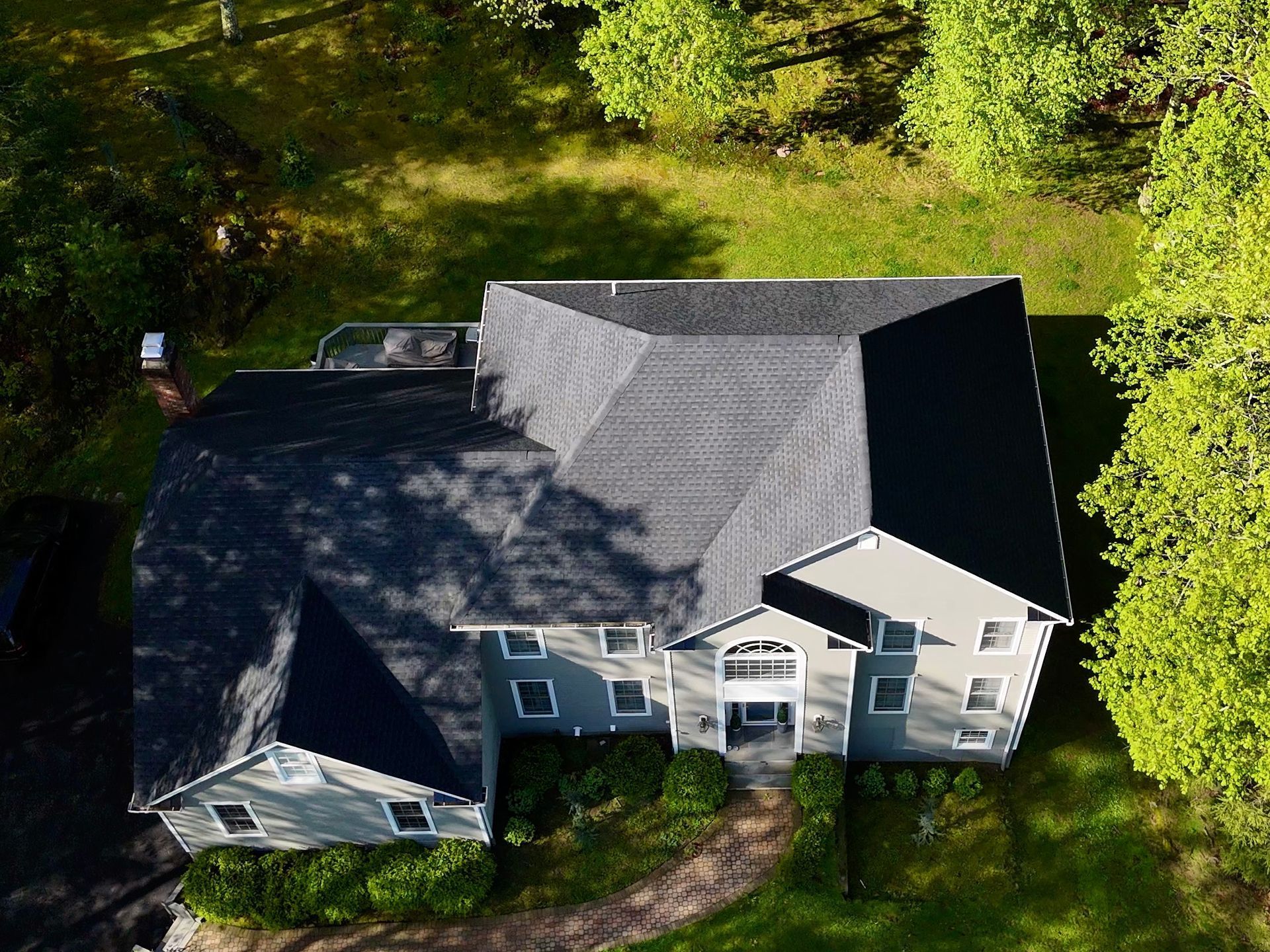 Aerial view of a gray house with a dark roof surrounded by green trees and grass.