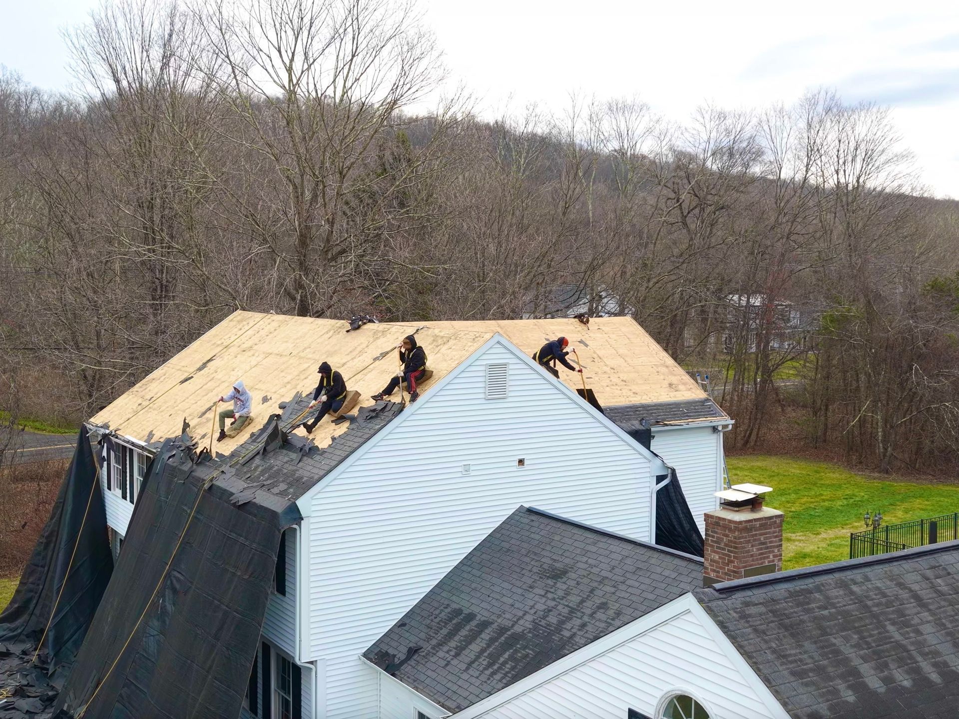 Roofers working on a house roof with a tarp covering part of the home.