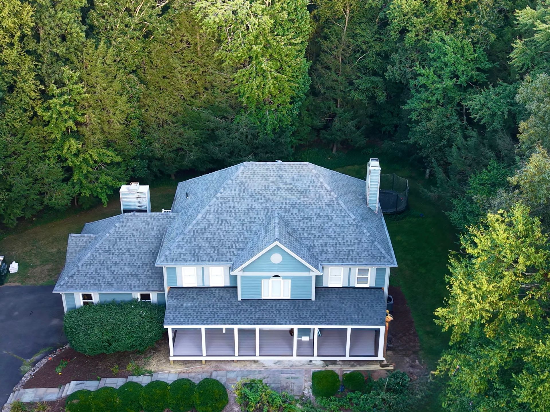 Aerial view of a blue-gray house with a porch, surrounded by lush green trees.