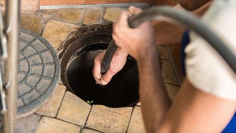 A man is cleaning a manhole with a hose.