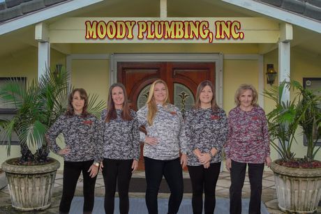 A group of women standing in front of a building that says moody plumbing inc.