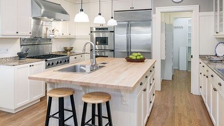 A kitchen with white cabinets , stainless steel appliances , a sink , and a large island.