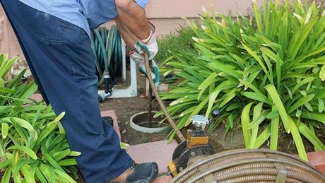 A man is using a hose to clean a drain in a garden.