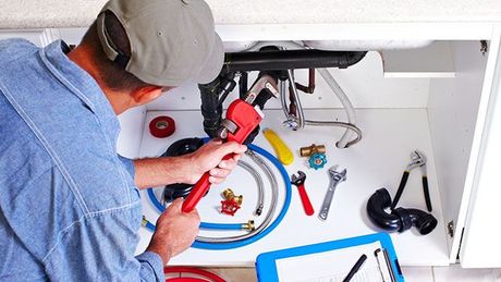 A plumber is fixing a sink in a kitchen with a wrench.