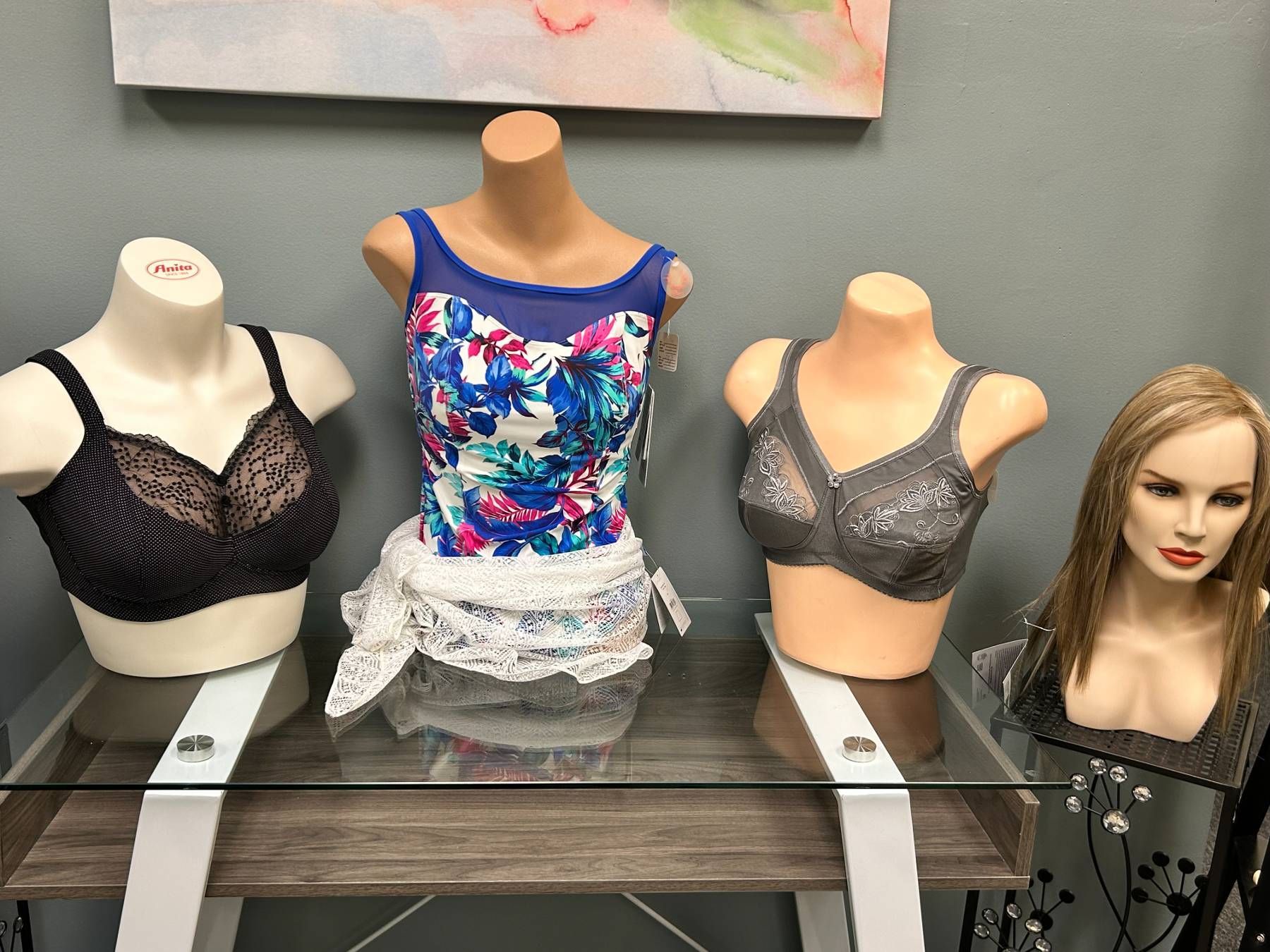 Three mannequins wearing bras and wigs are sitting on a glass table.