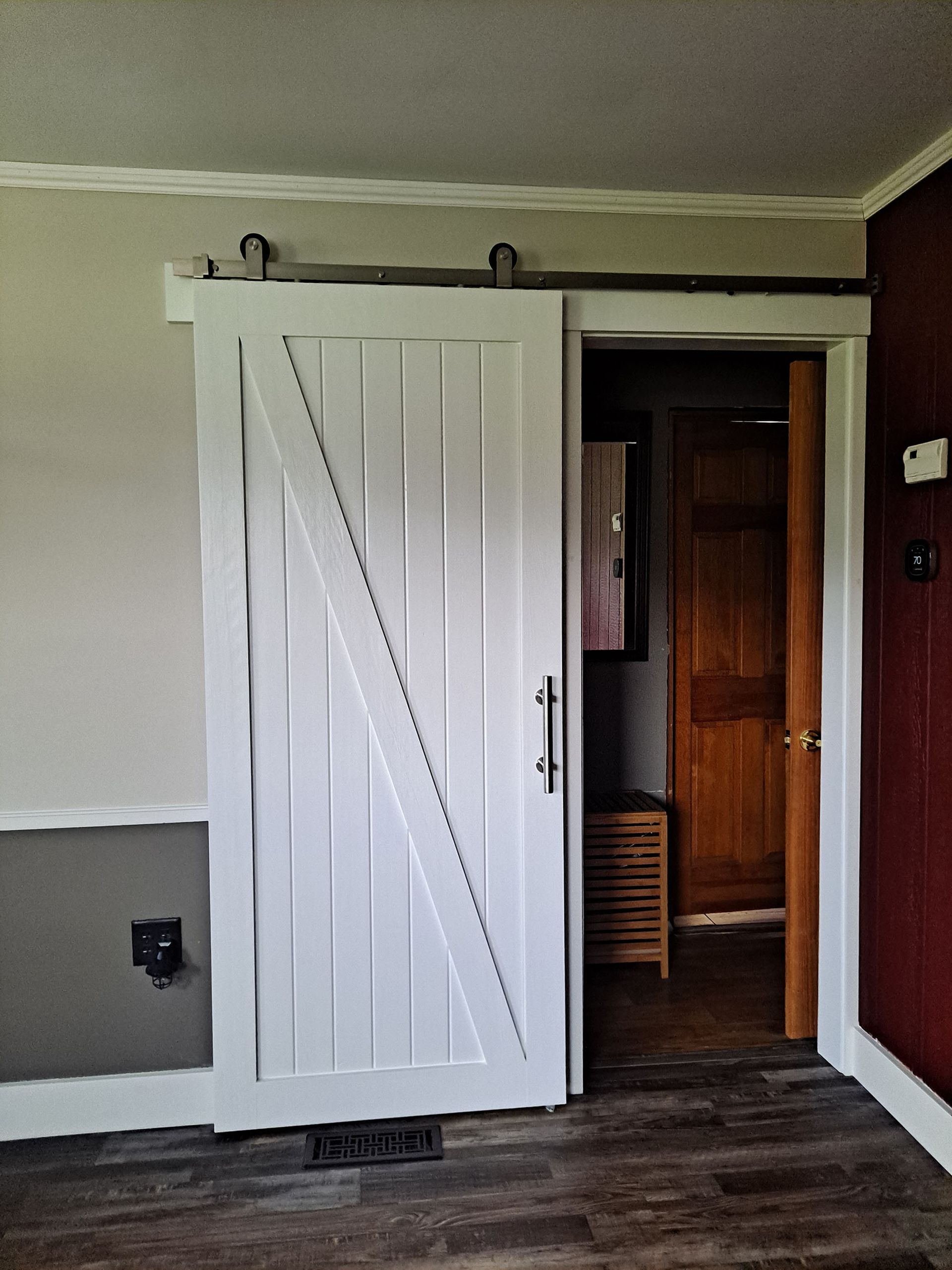 White barn door on a black track, leading into a room with a wooden door.