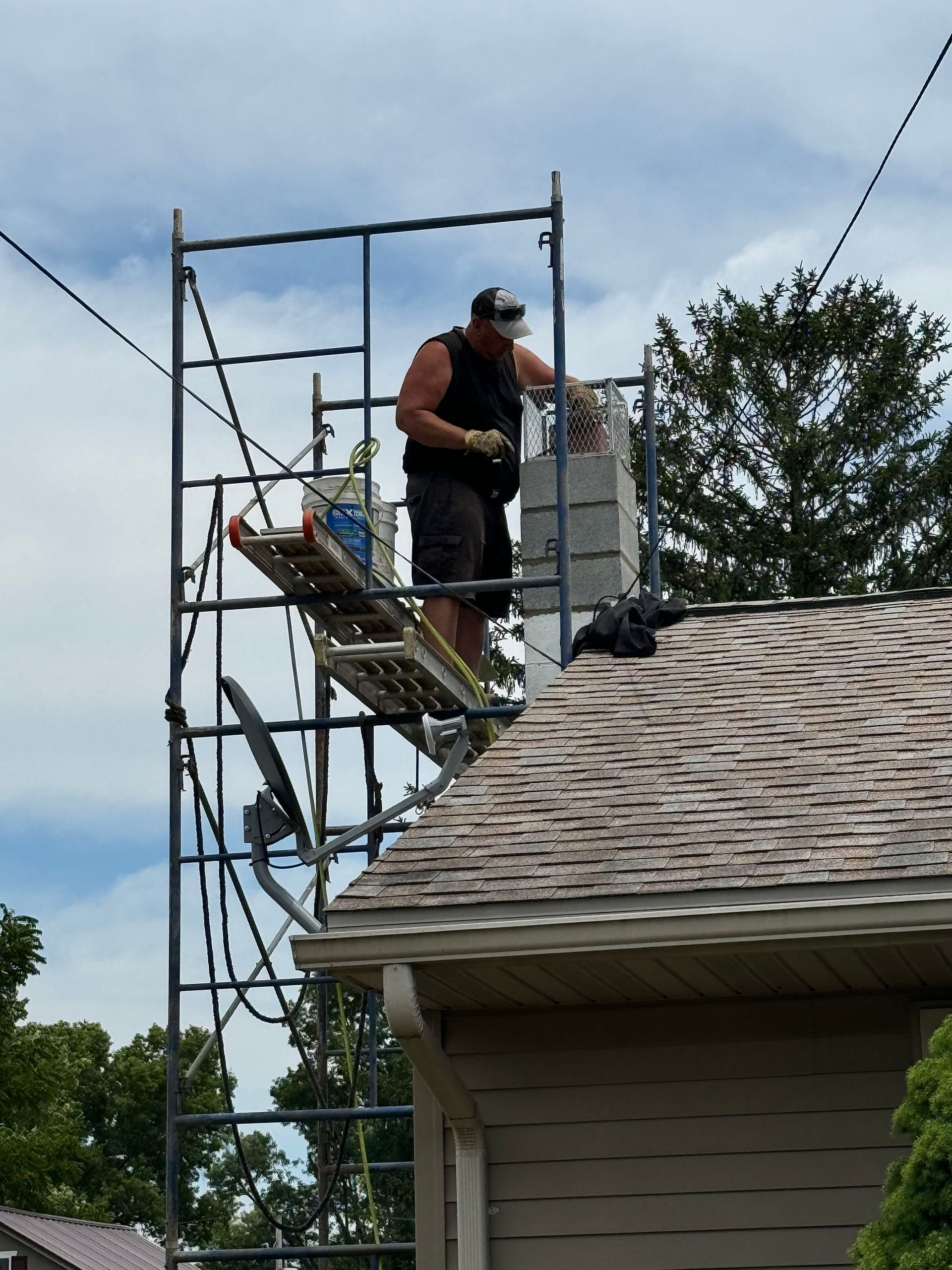 Person on scaffolding working on a chimney on a roof, blue sky backdrop.