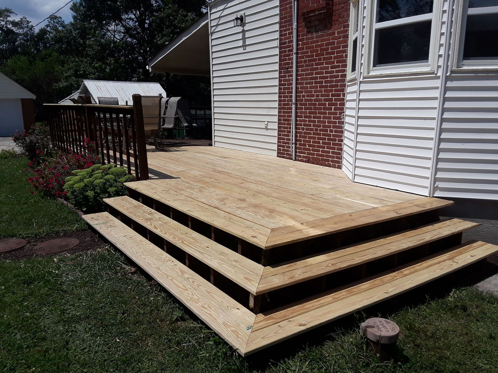 Wooden deck with three steps, attached to a white-sided house and surrounded by green grass.