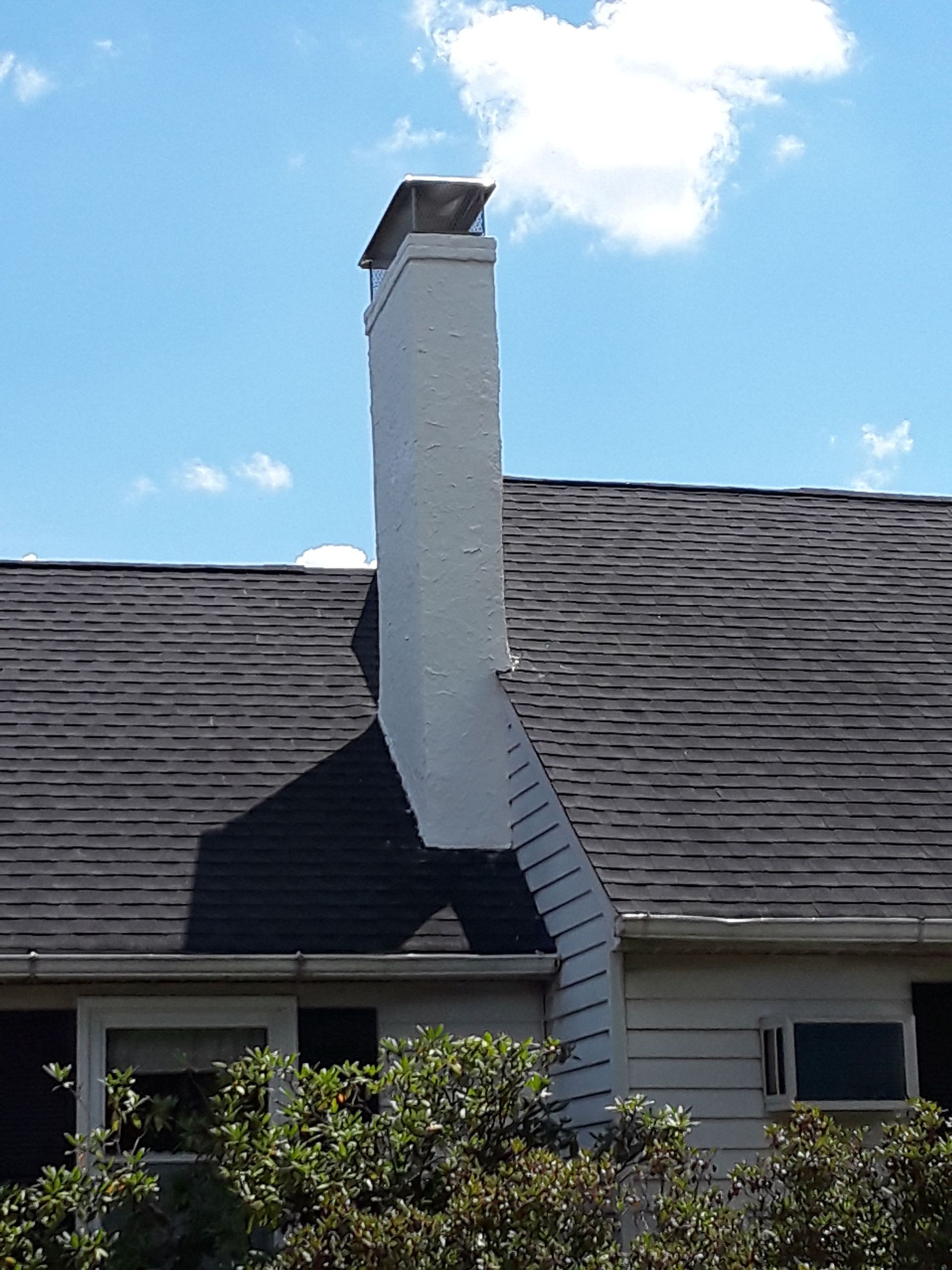 White chimney on a dark roof against a blue sky with a few clouds.