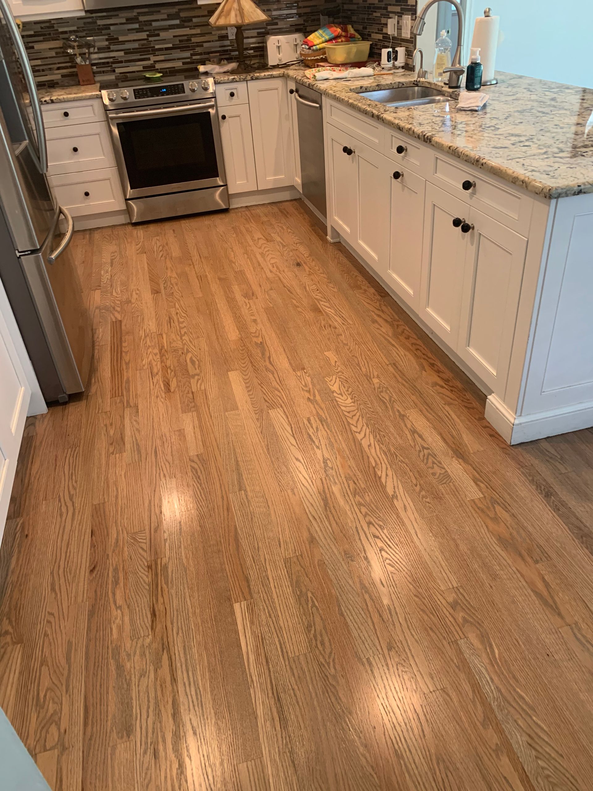 A kitchen with hardwood floors , white cabinets and stainless steel appliances.