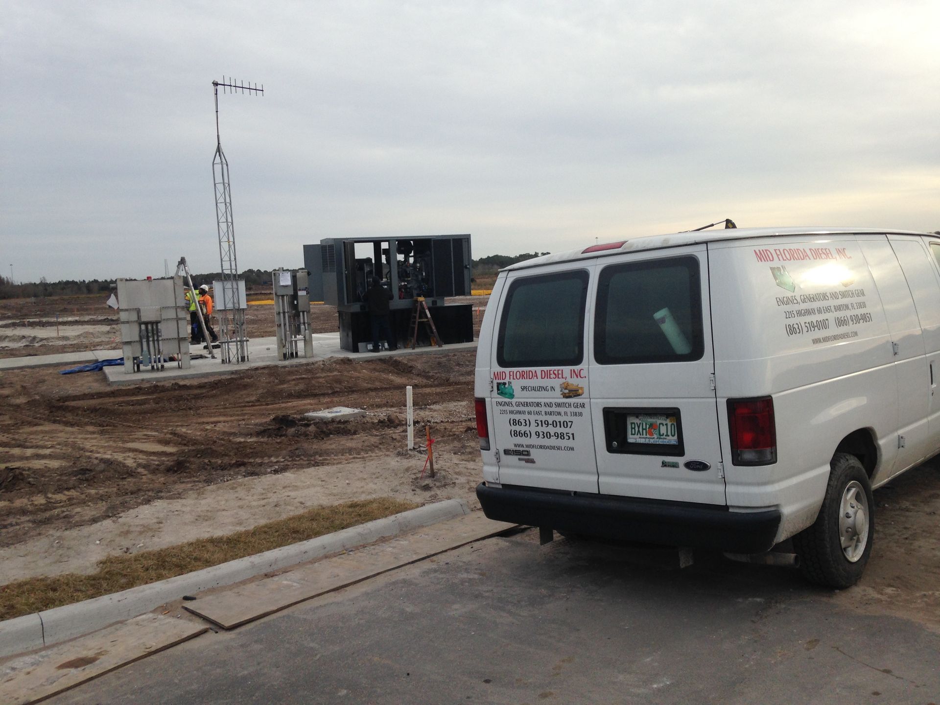 White work van parked by a muddy construction site with workers and equipment in the background