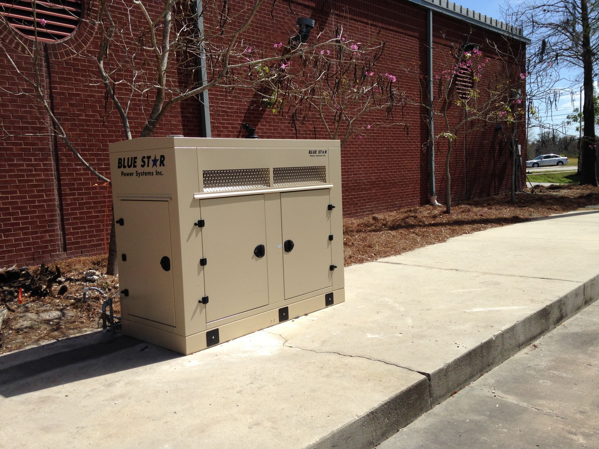Beige utility box beside a red brick building along a sidewalk